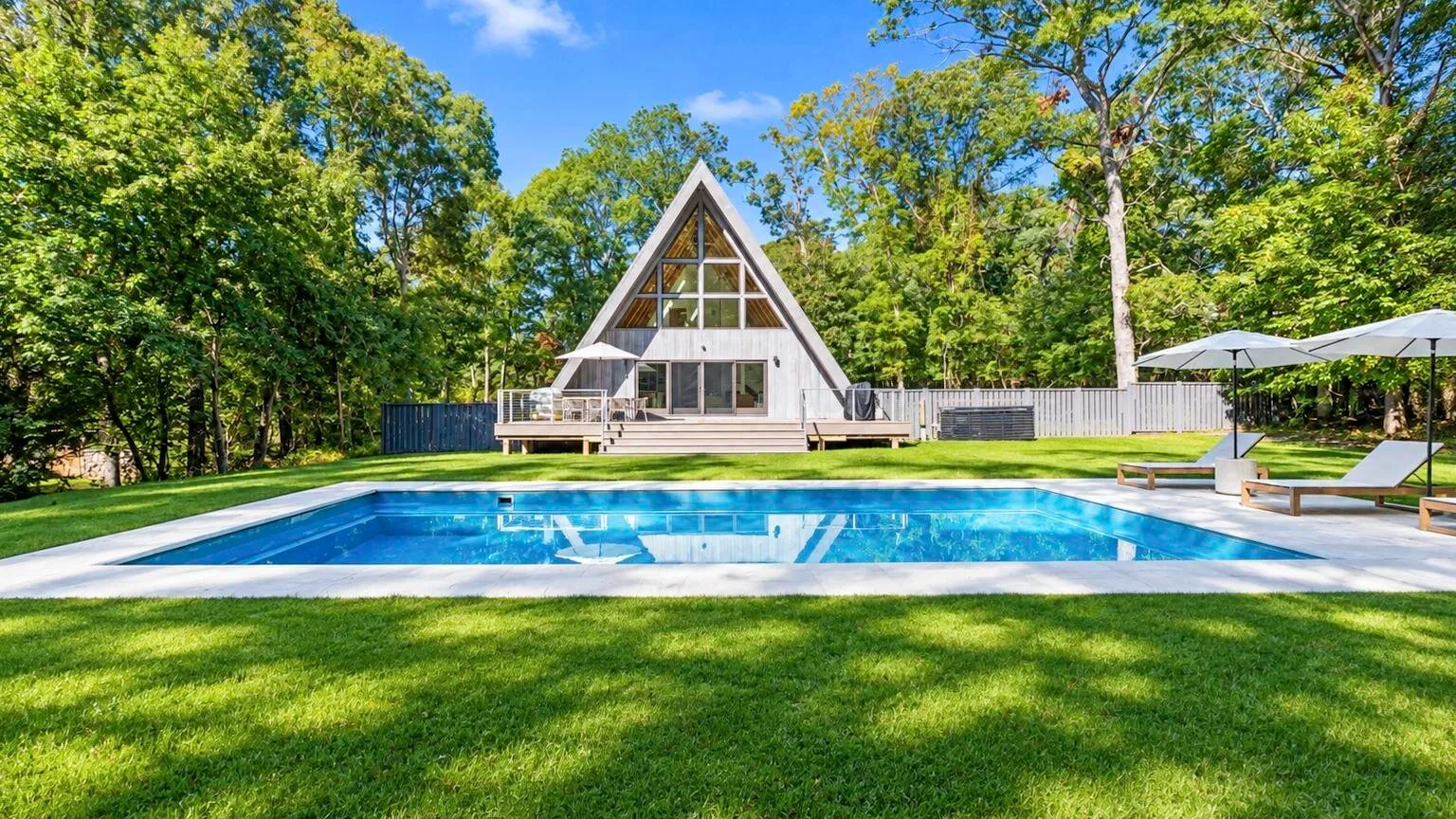 A-frame house and outdoor swimming pool set in a tree-lined yard.