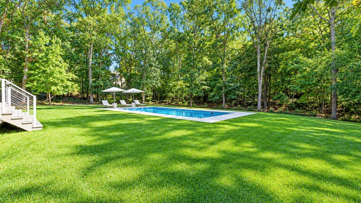 A swimming pool sits beside a broad lawn, surrounded by leafy trees.