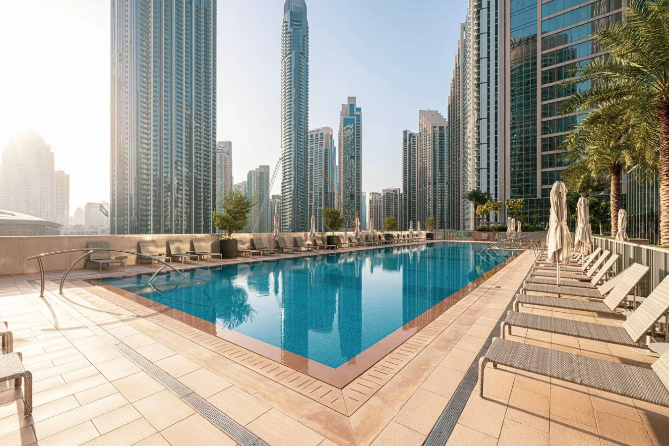 Una piscina en la azotea está rodeada de tumbonas y edificios altos.