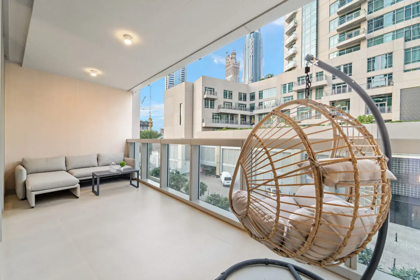 A covered balcony seating area with a hanging chair and views of nearby buildings.