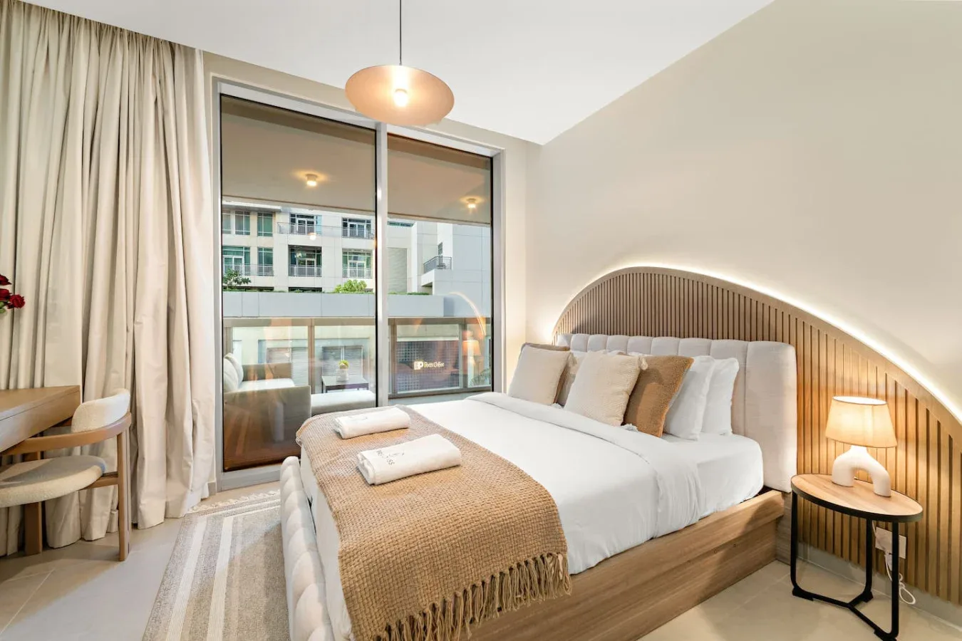 Un dormitorio con una cama tendida junto a grandes ventanas y cortinas.