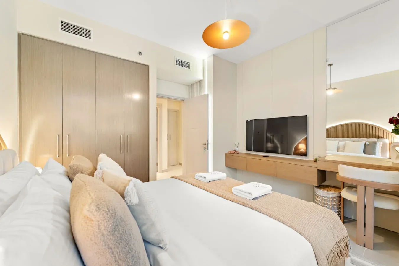 Un dormitorio luminoso con una cama bien tendida y un televisor sobre un mueble bajo.