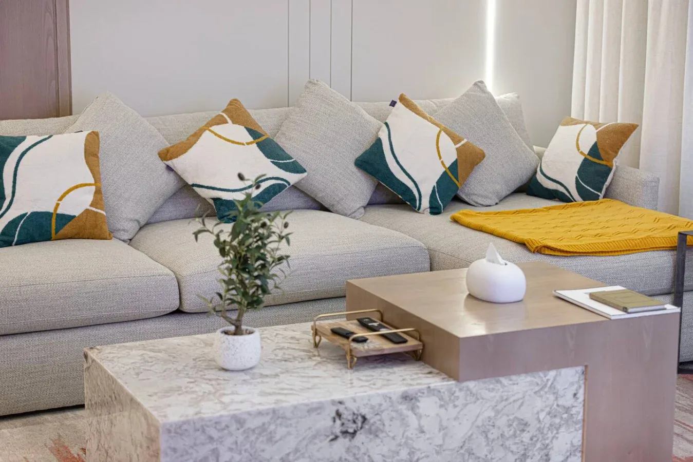 Una sala luminosa con un sofá seccional claro y una mesa de centro de mármol.