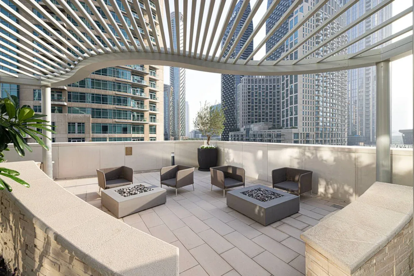 Una terraza en la azotea con asientos al aire libre bajo una cubierta de listones, con edificios cercanos a la vista.