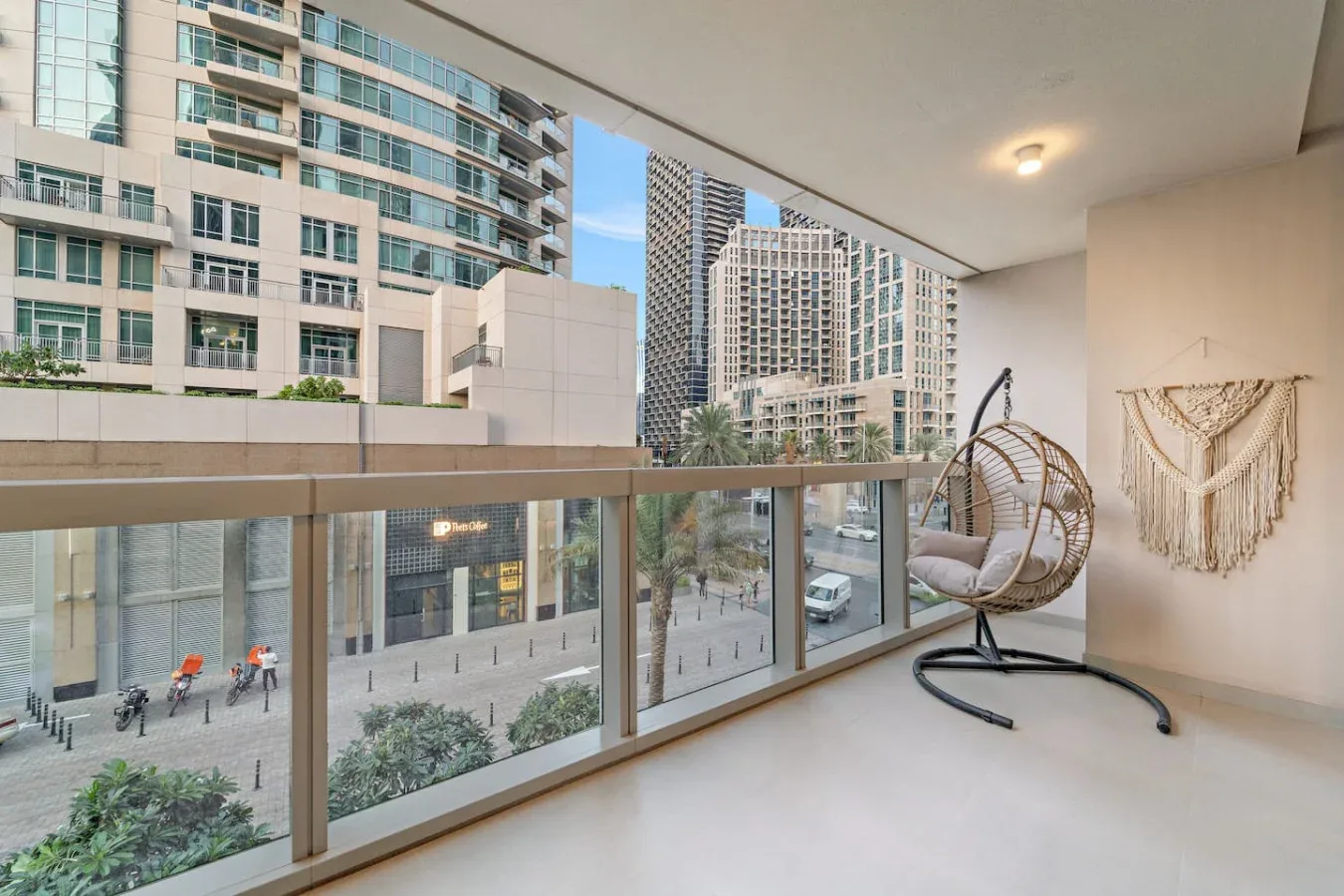 Un balcón con un asiento colgante tiene vistas a edificios urbanos y una calle peatonal.
