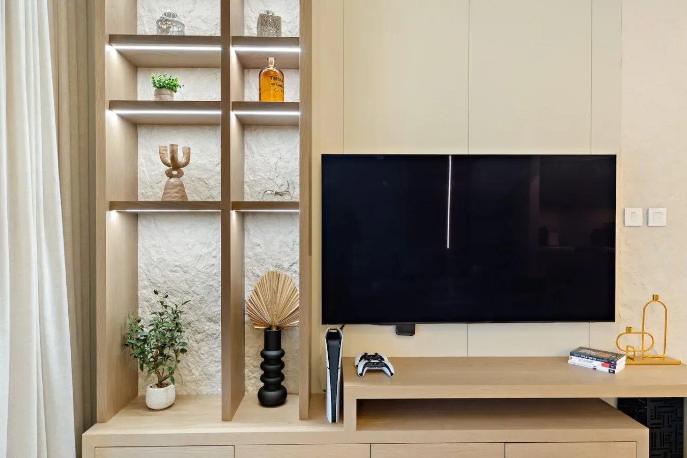 Una pared de sala de estar presenta un televisor grande sobre un mueble bajo de madera.