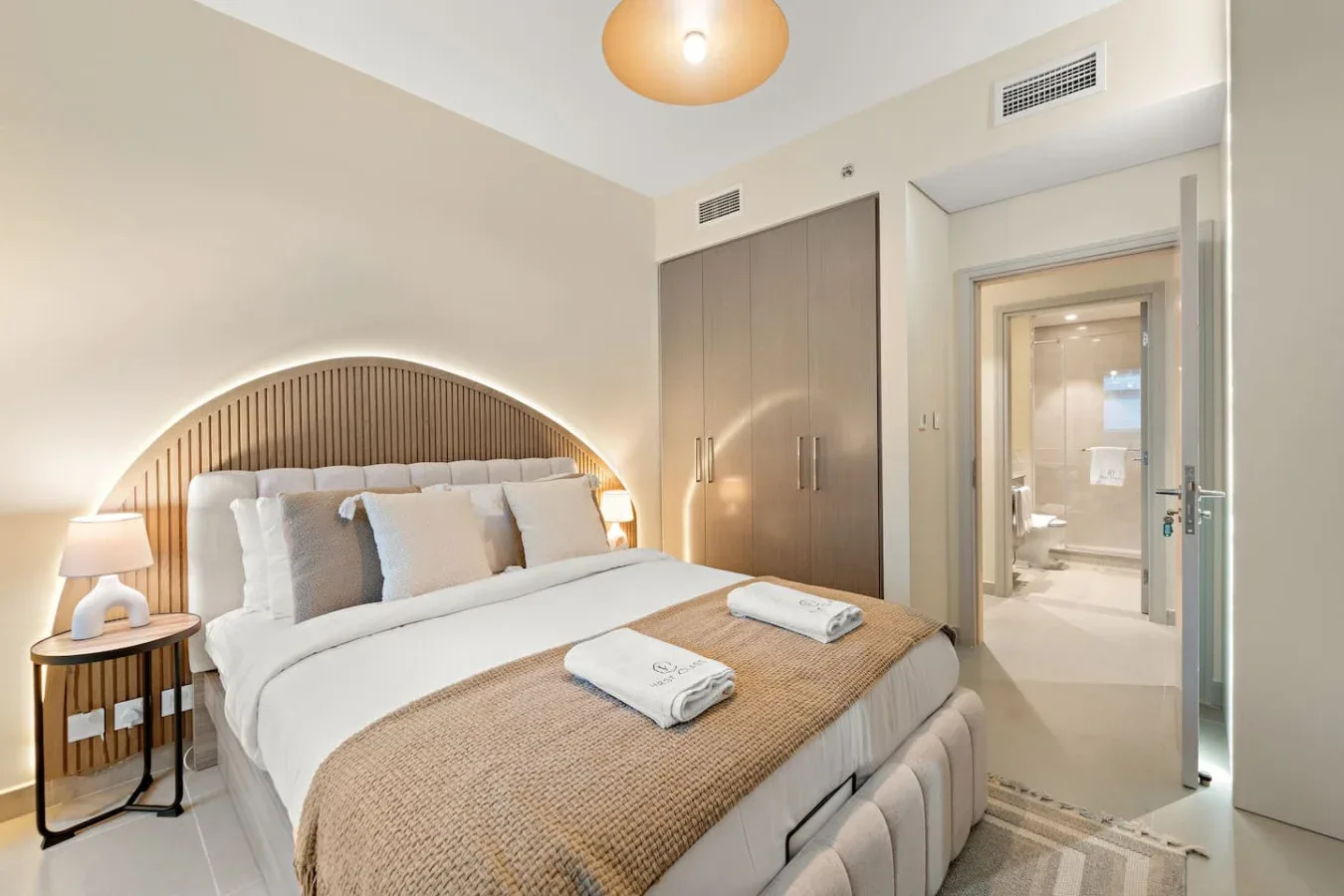 Un dormitorio luminoso con una cama bien tendida y una puerta al baño.