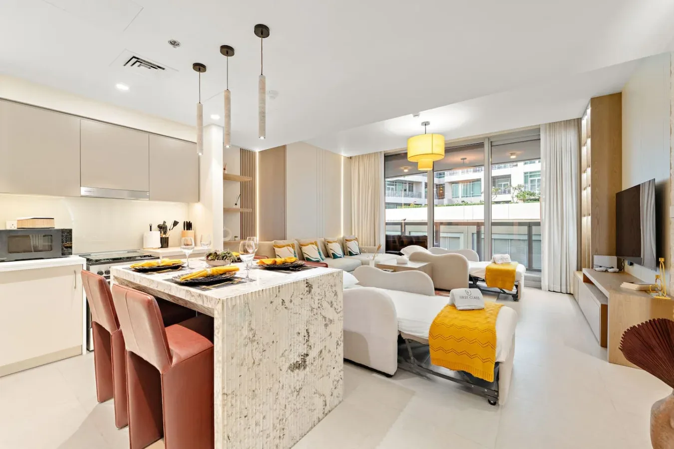 Una cocina y sala de estar de planta abierta incluye una isla y asientos junto a grandes ventanales.