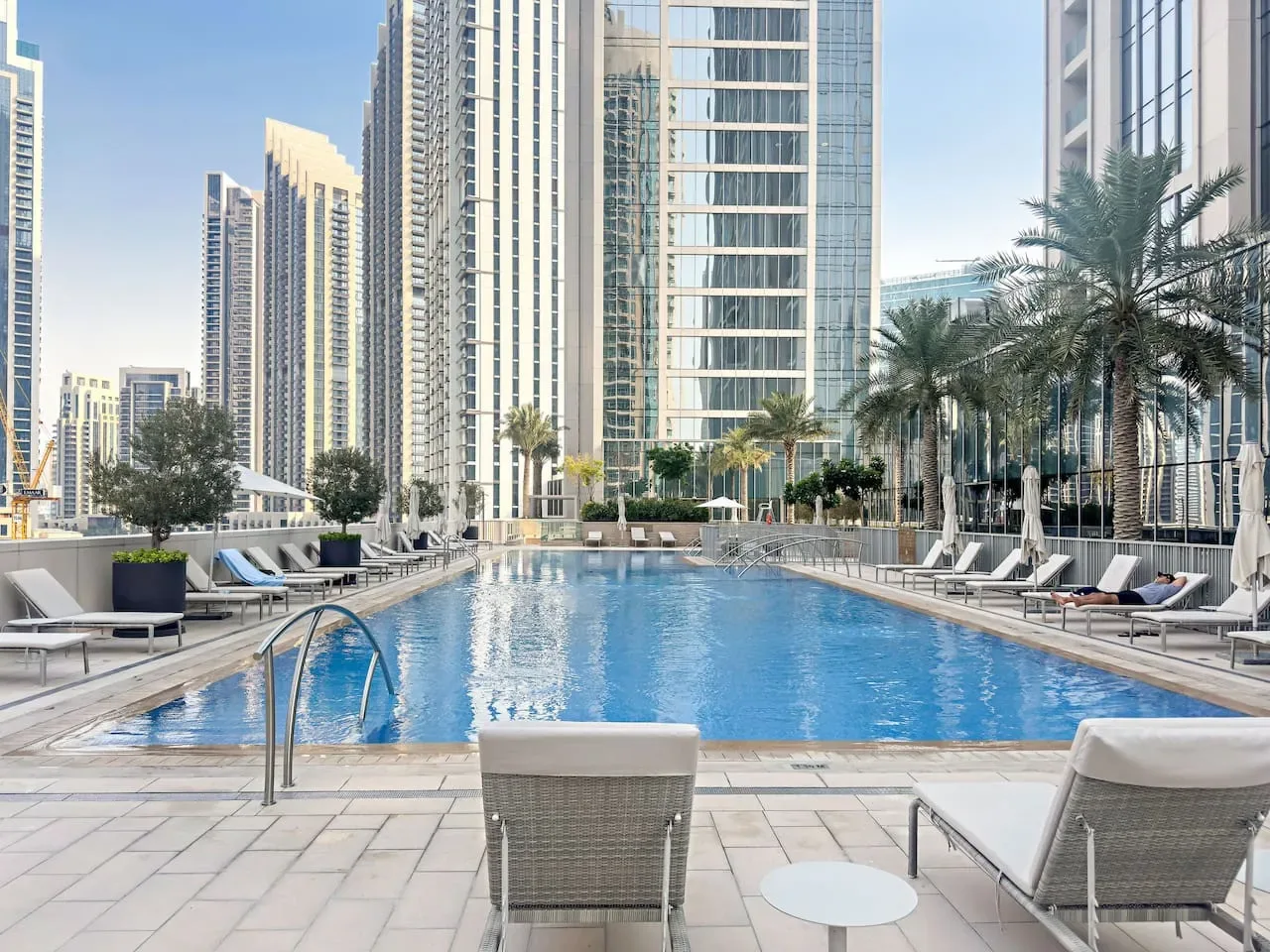 An outdoor swimming pool with lounge seating and tall buildings in the background.