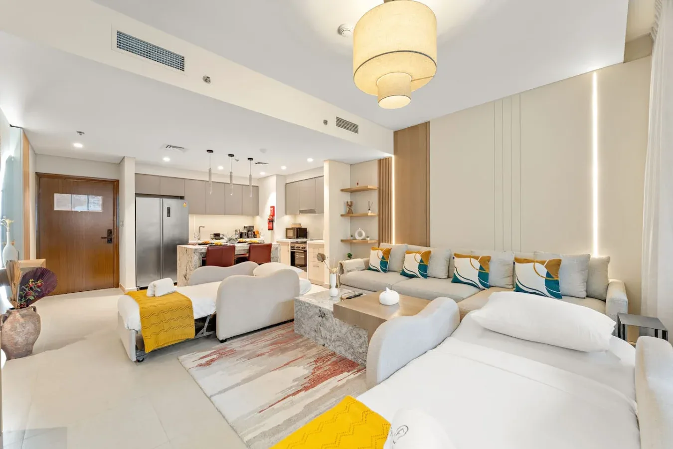 Una sala luminosa con asientos blancos y una cocina abierta al fondo.
