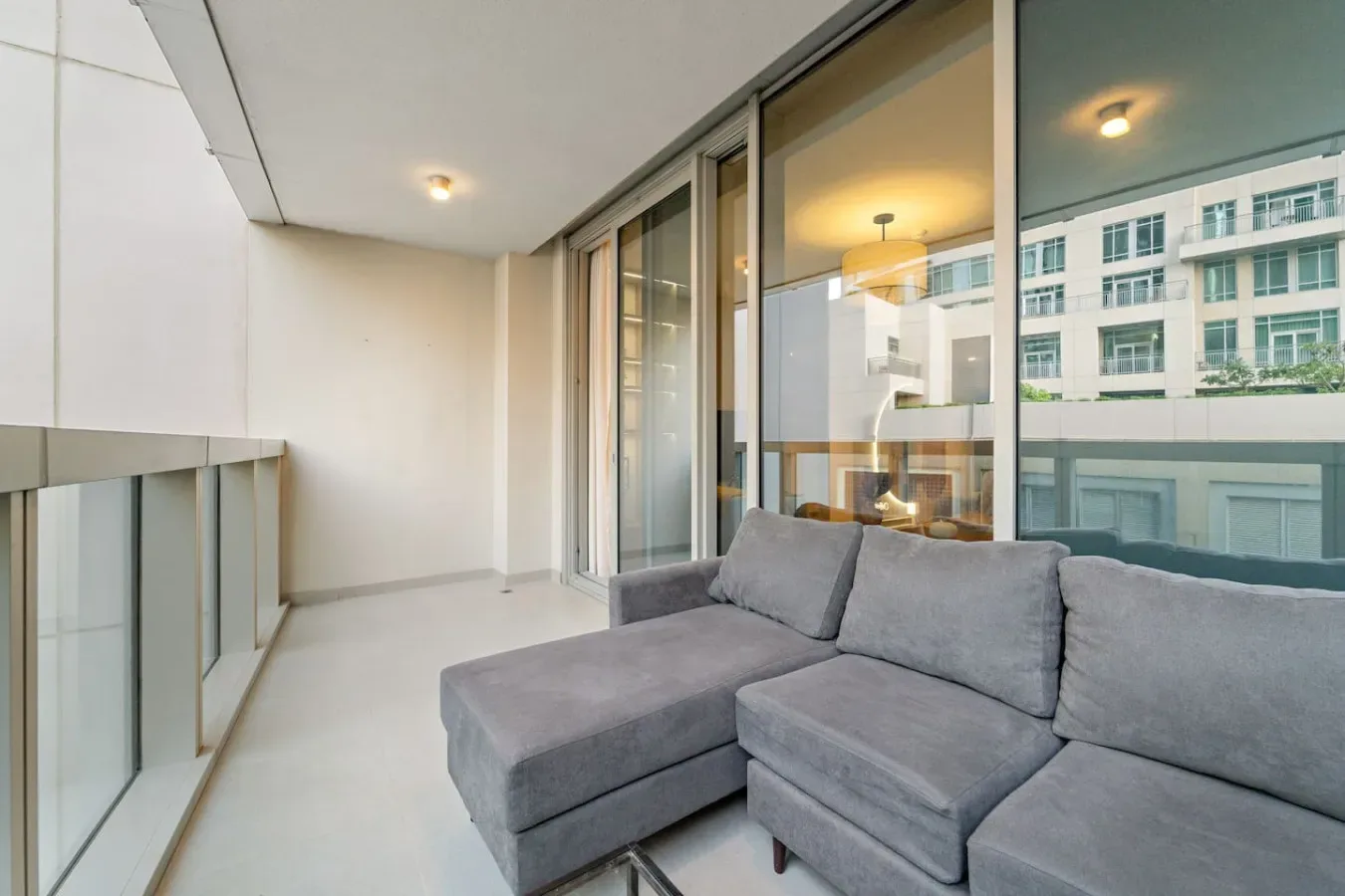 A covered balcony with gray seating and glass doors overlooking nearby buildings.