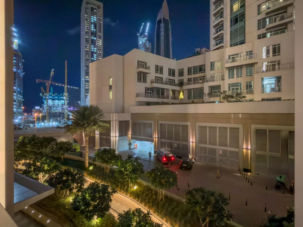 Un edificio de varios pisos da a un patio ajardinado y una calle de noche.