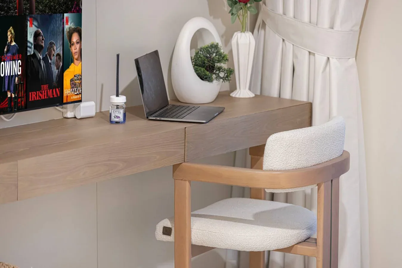 Un escritorio con una computadora portátil y una silla acolchada está junto a una ventana con cortinas.