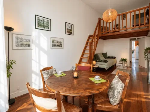 Suite con entreplanta, mesa de comedor, escalera de madera y dormitorio en el nivel superior.