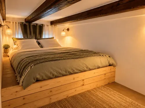 Dormitorio en la entreplanta con vigas de madera vistas y suelo de madera.