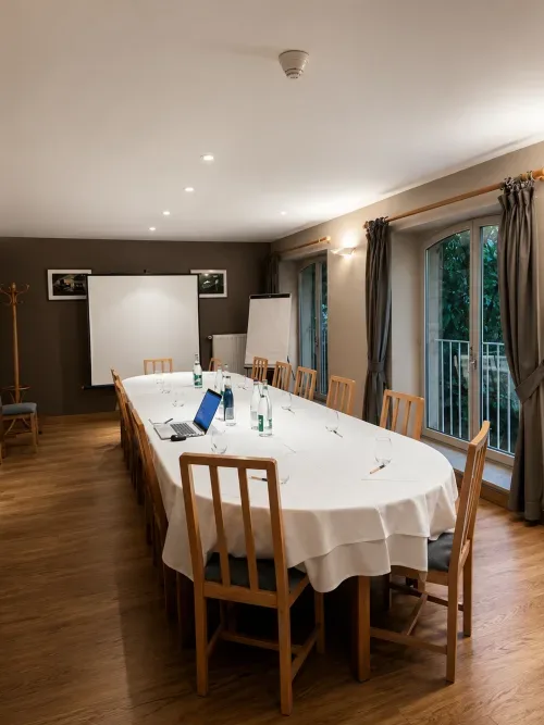 Sala de reuniones con mesa ovalada, sillas de madera, pantalla de proyección y vistas al jardín.