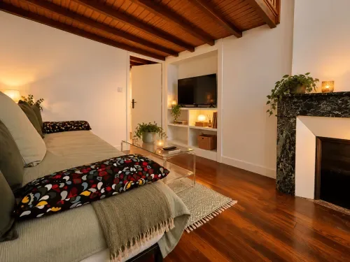 Suite con entreplanta, vigas vistas, cama, chimenea, televisión y plantas.