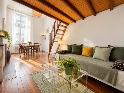 Suite con entreplanta, vigas vistas, sofá, zona de comedor y escalera de madera.