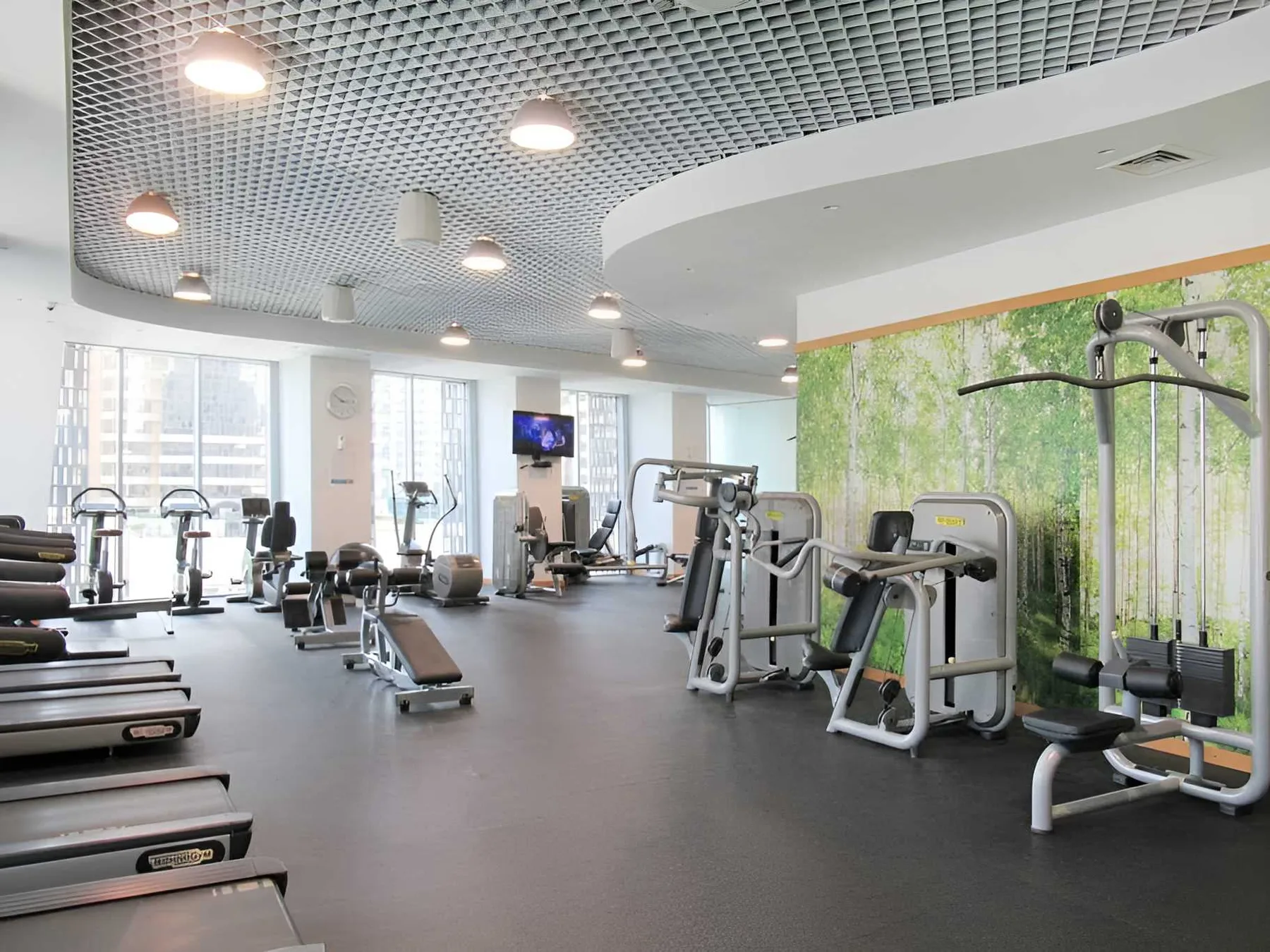 Un gimnasio con máquinas de ejercicio y grandes ventanales.