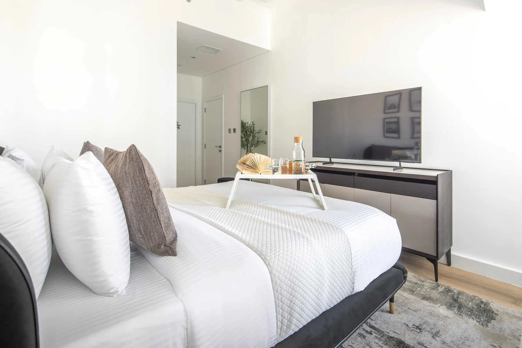 Un dormitorio luminoso con ropa de cama blanca y un televisor sobre un mueble bajo.