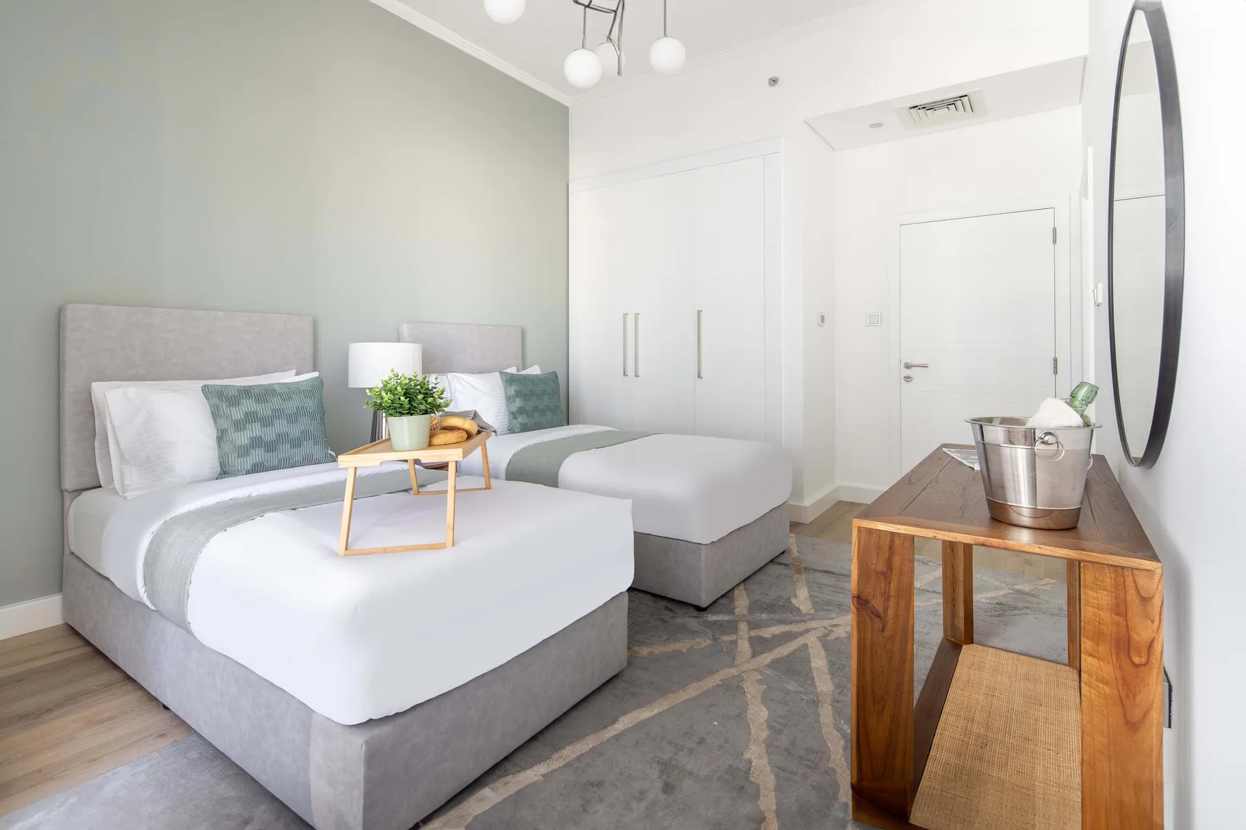 Un dormitorio luminoso con dos camas, una consola de madera y un gran espejo de pared.