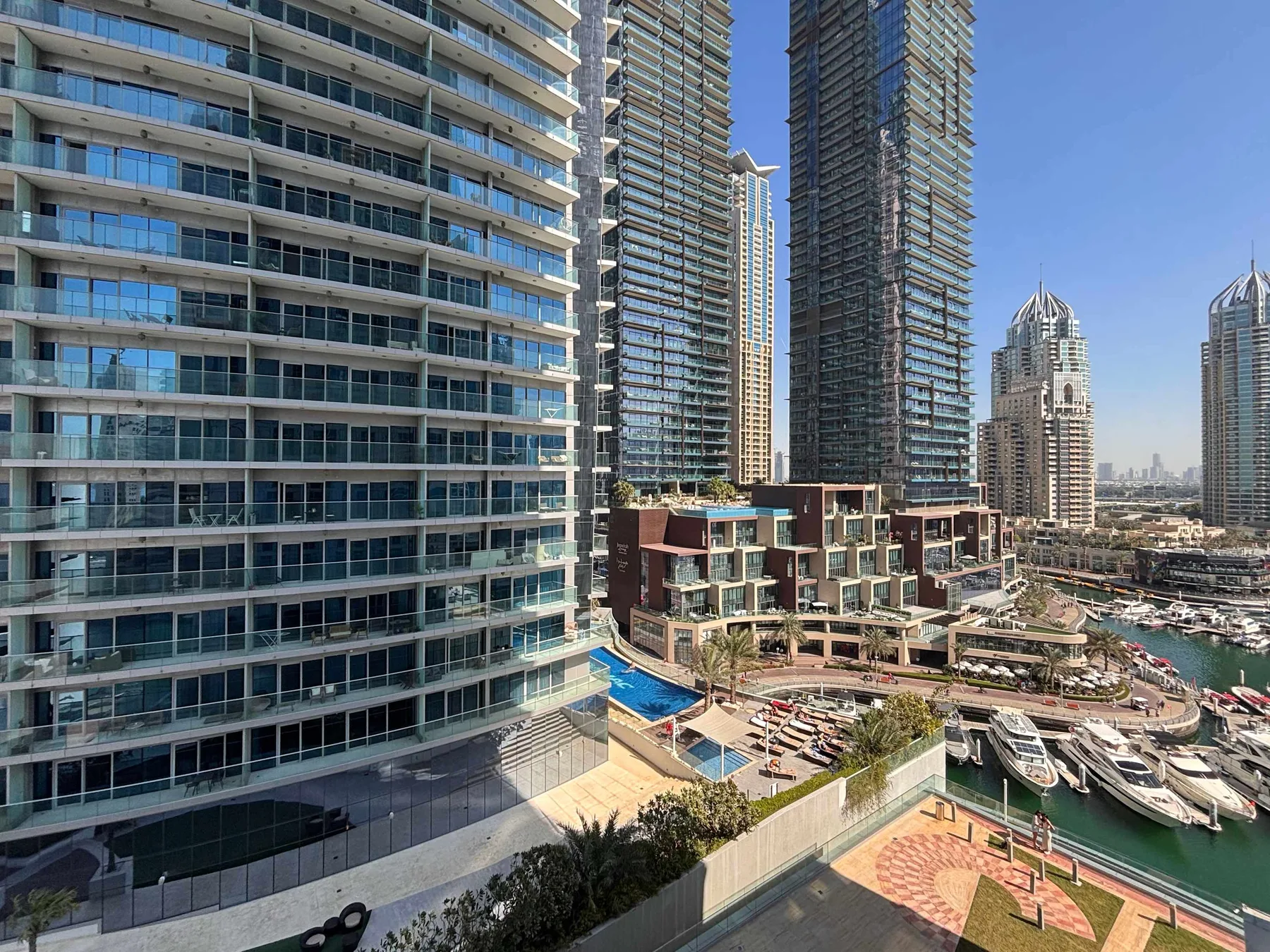 Edificios modernos de gran altura dan a una zona costera ajardinada con piscina y embarcaciones.