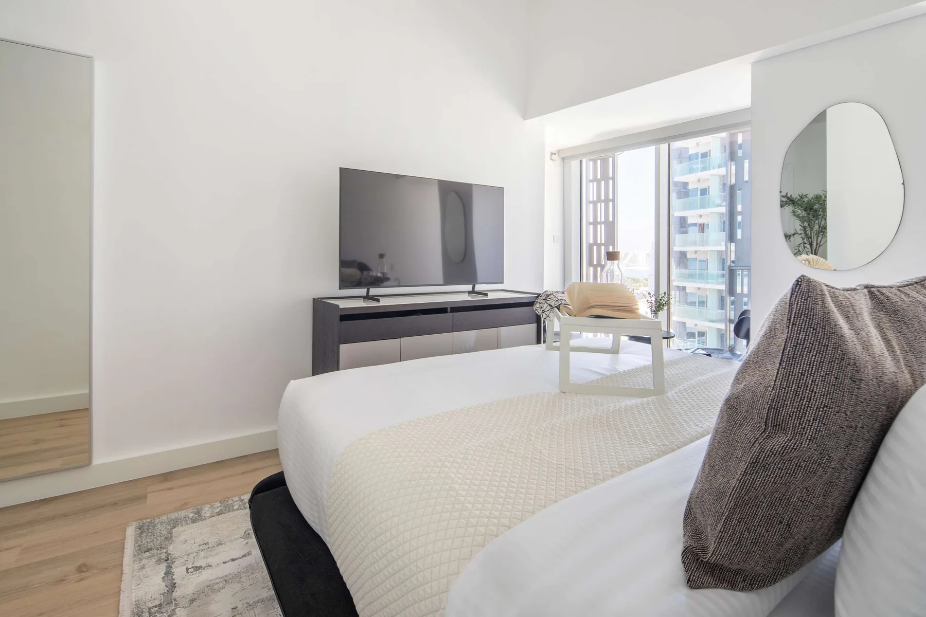 Un dormitorio luminoso con cama, televisor y ventanales.