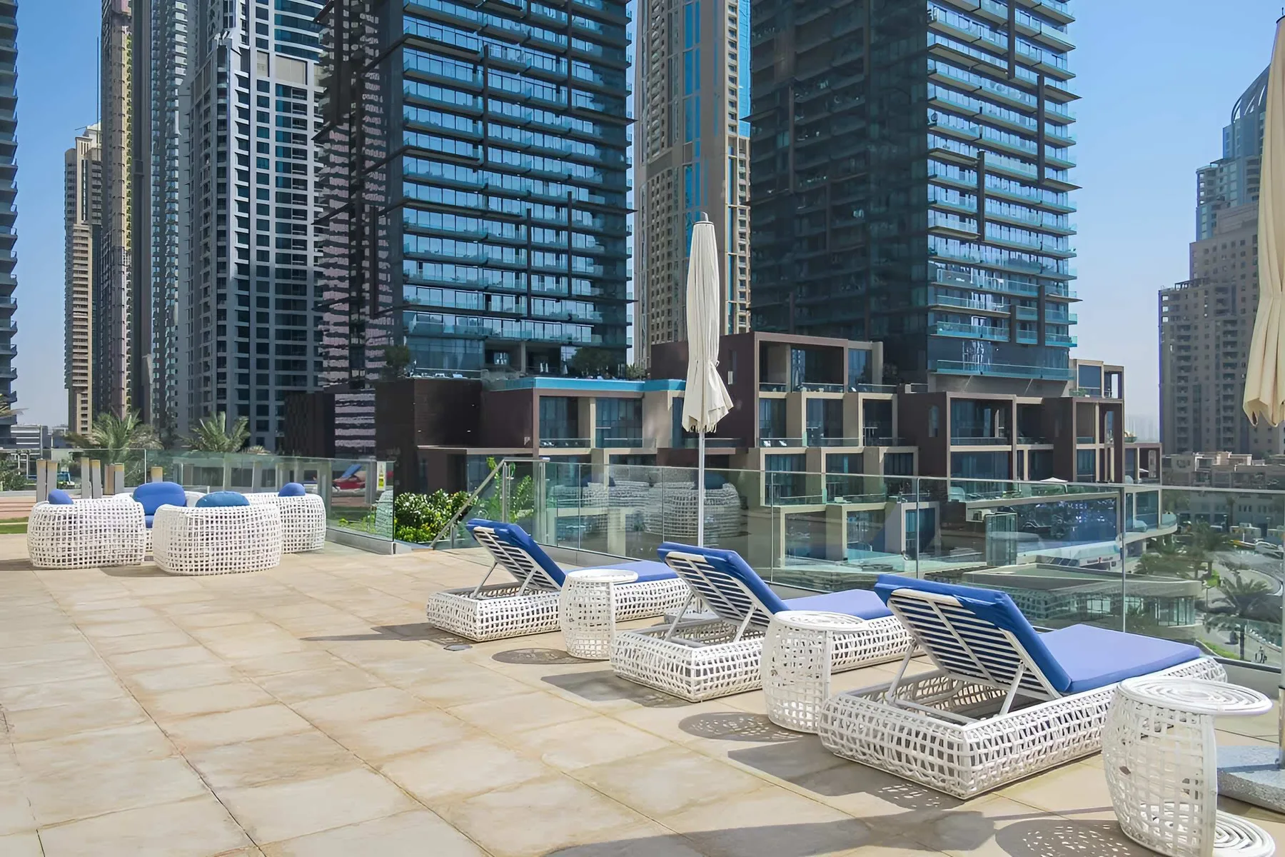 Una terraza con piscina, tumbonas blancas y edificios altos al fondo.
