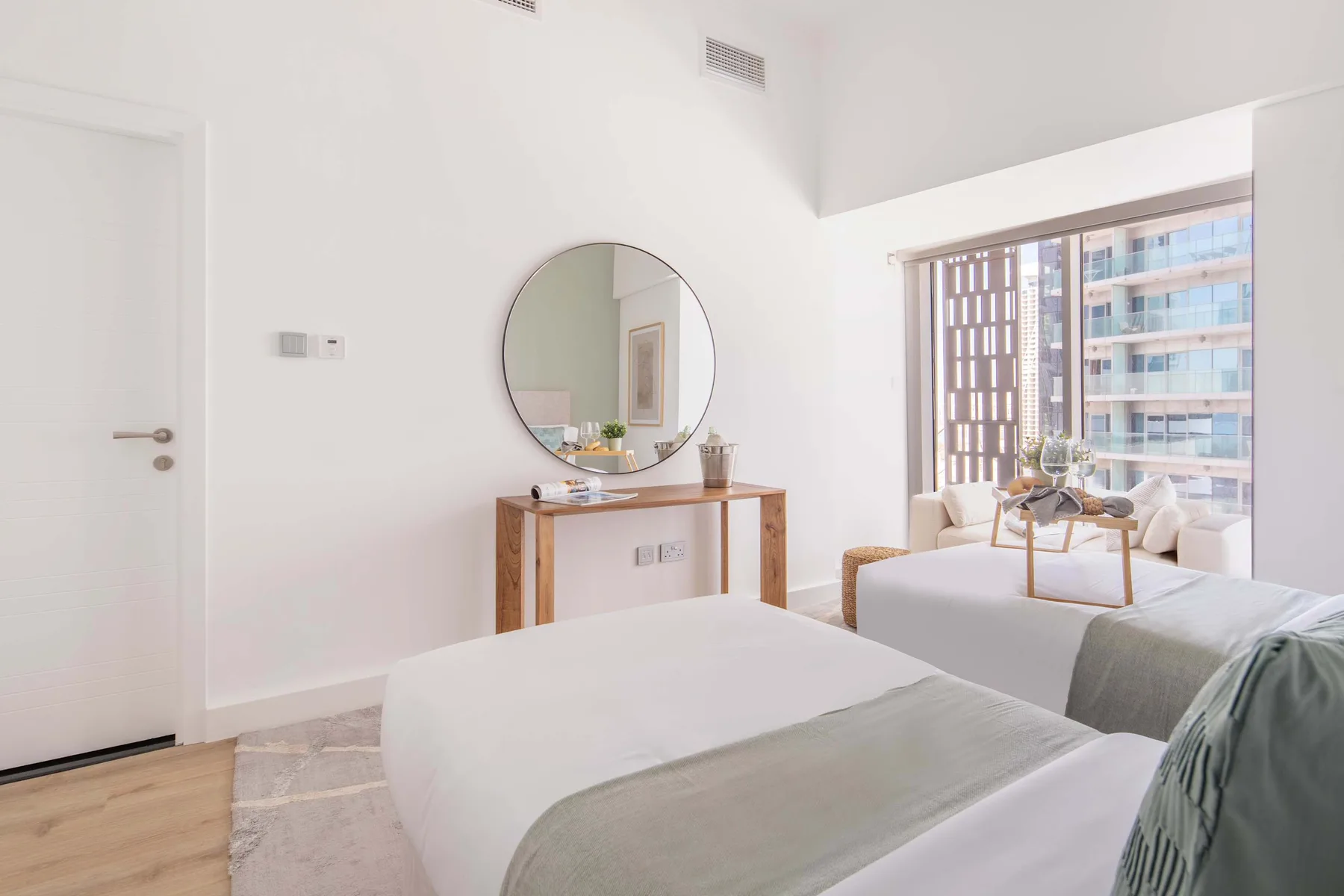 Un dormitorio luminoso con dos camas y un espejo redondo sobre una cómoda.