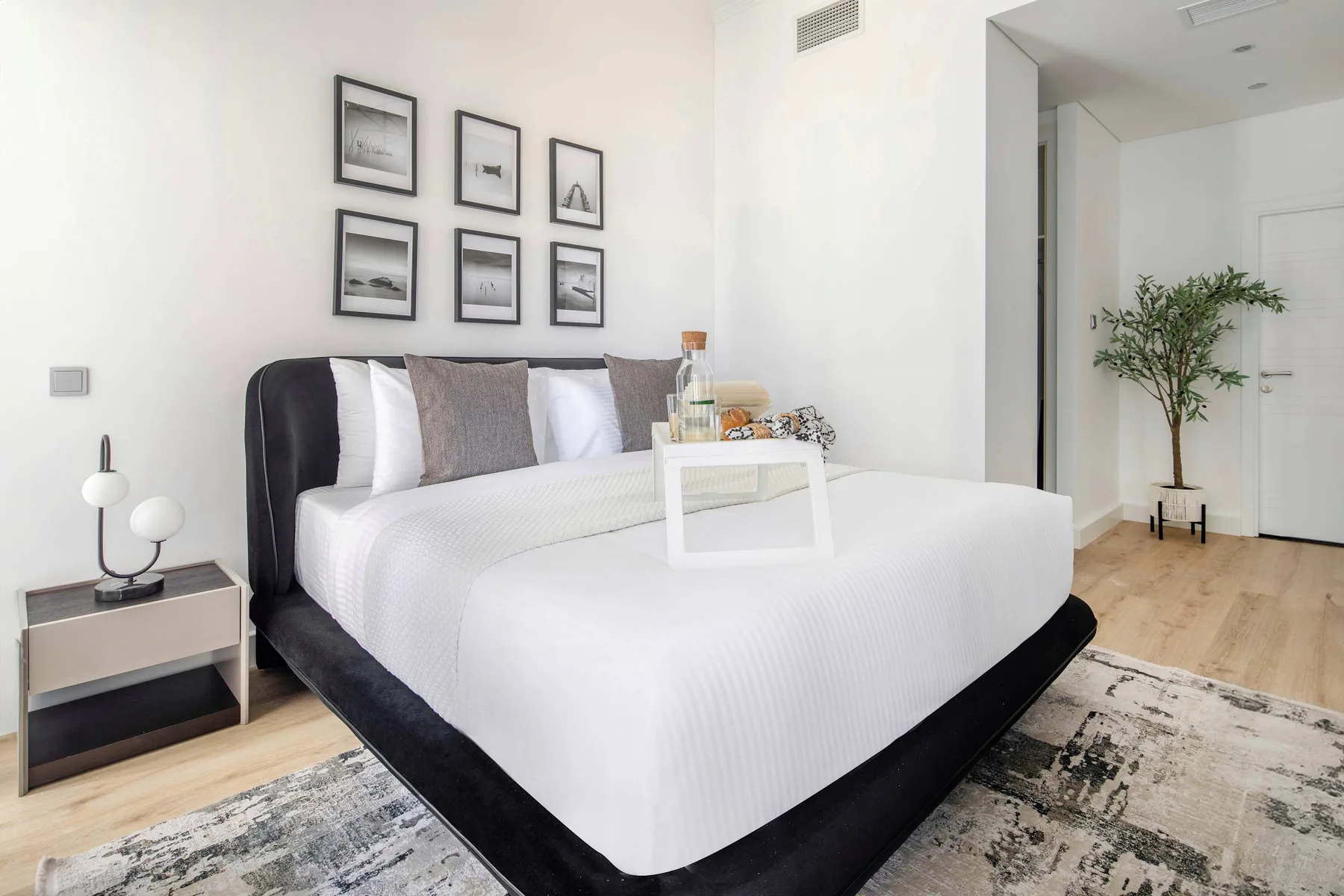 Un dormitorio luminoso con una cama tendida y cuadros enmarcados encima.
