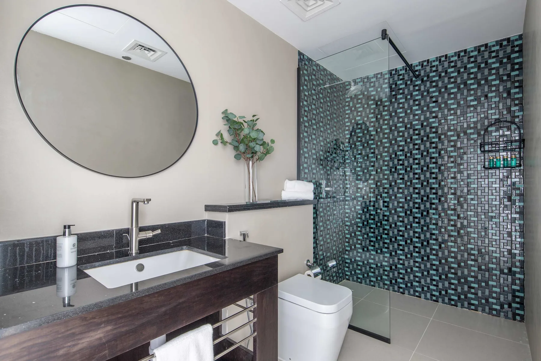 Un baño con lavabo, espejo redondo y zona de ducha con azulejos.