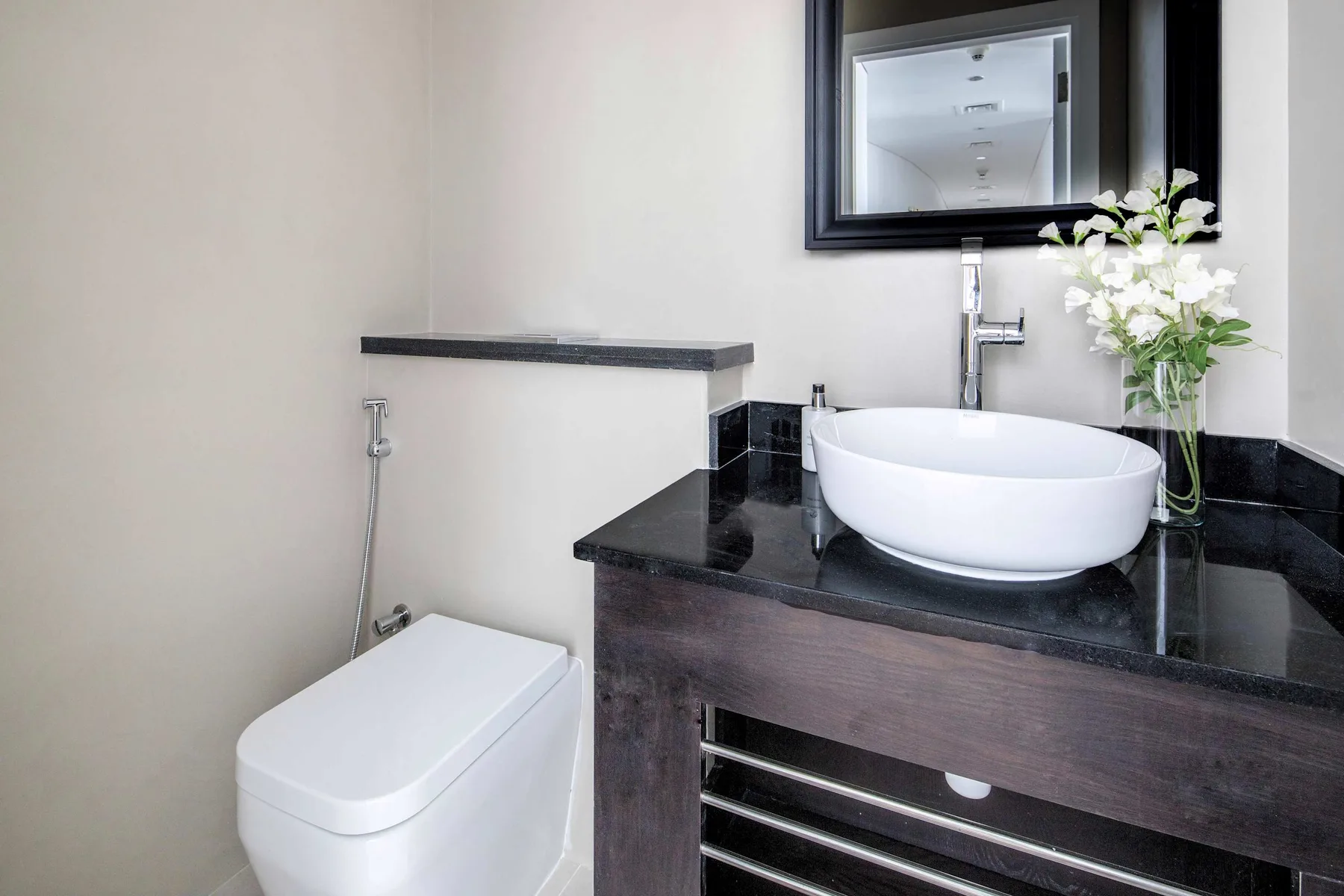 Un baño con un lavabo blanco sobre un tocador oscuro junto a un inodoro.