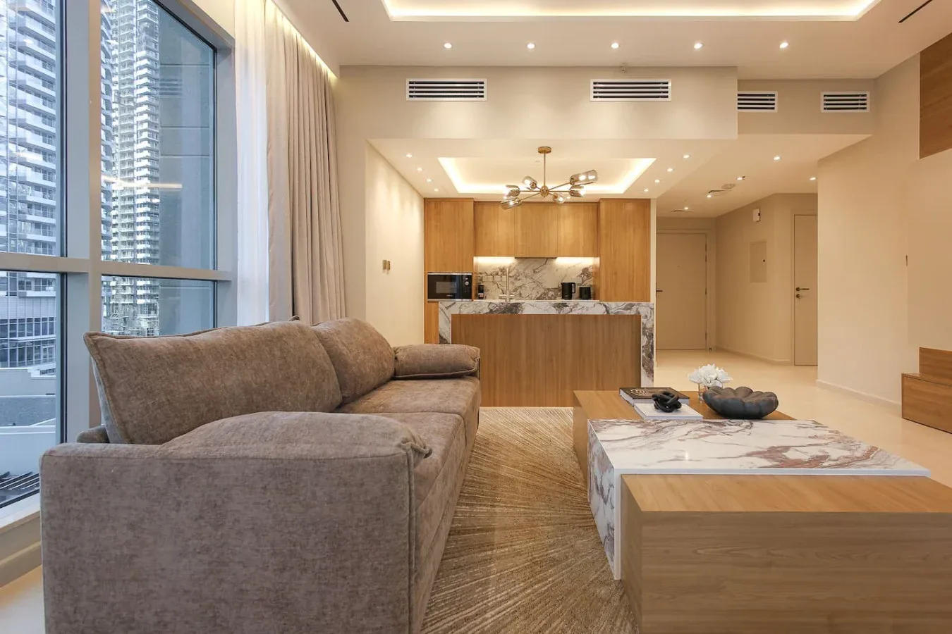 Una sala moderna con asientos junto a grandes ventanales y una cocina abierta.