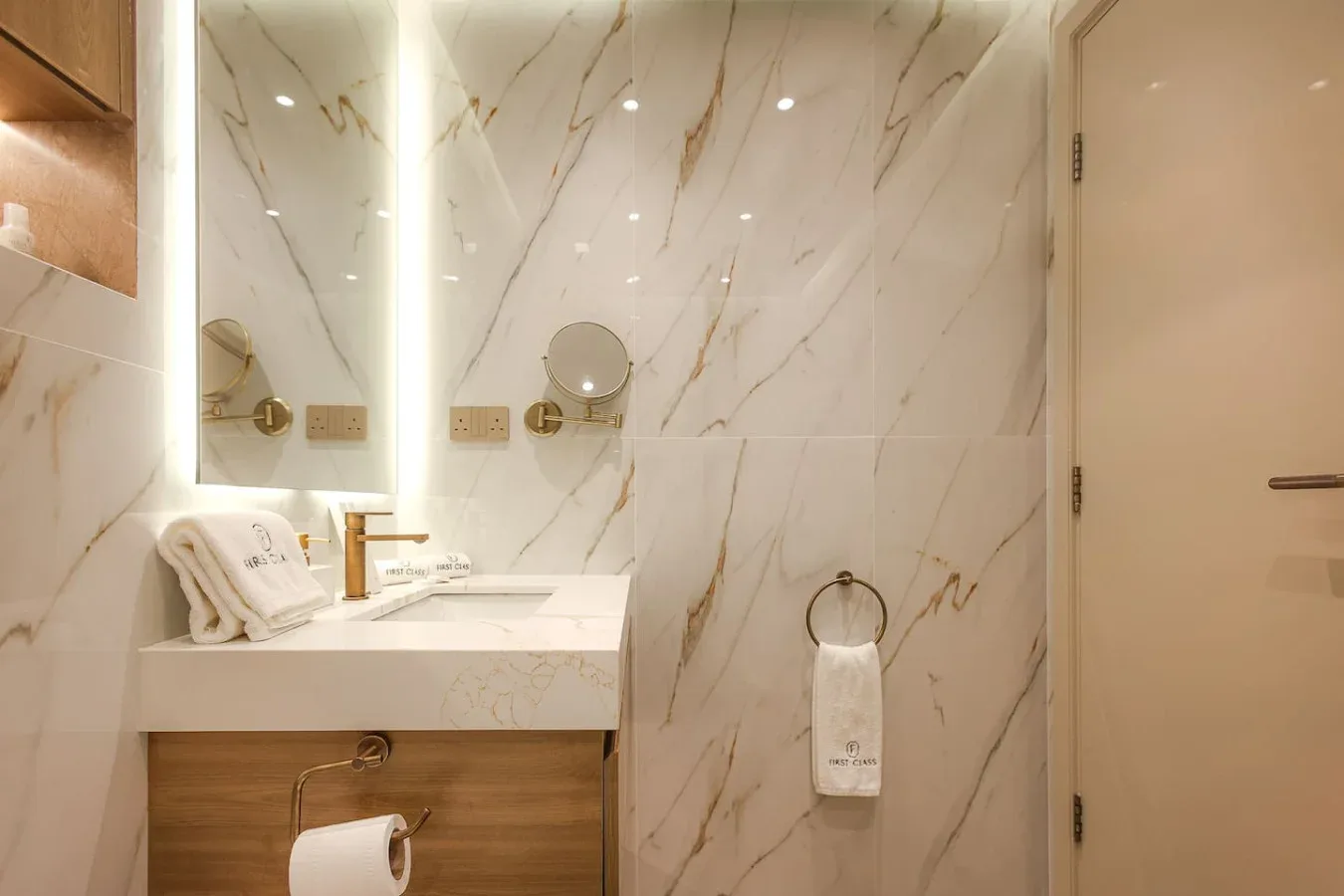 Un baño con azulejos de mármol, lavabo, espejo y aro para toalla.