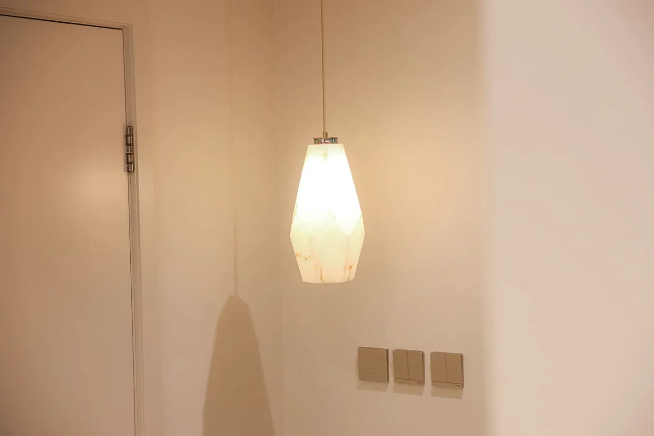Una lámpara colgante encendida está sobre interruptores, junto a una puerta cerrada.