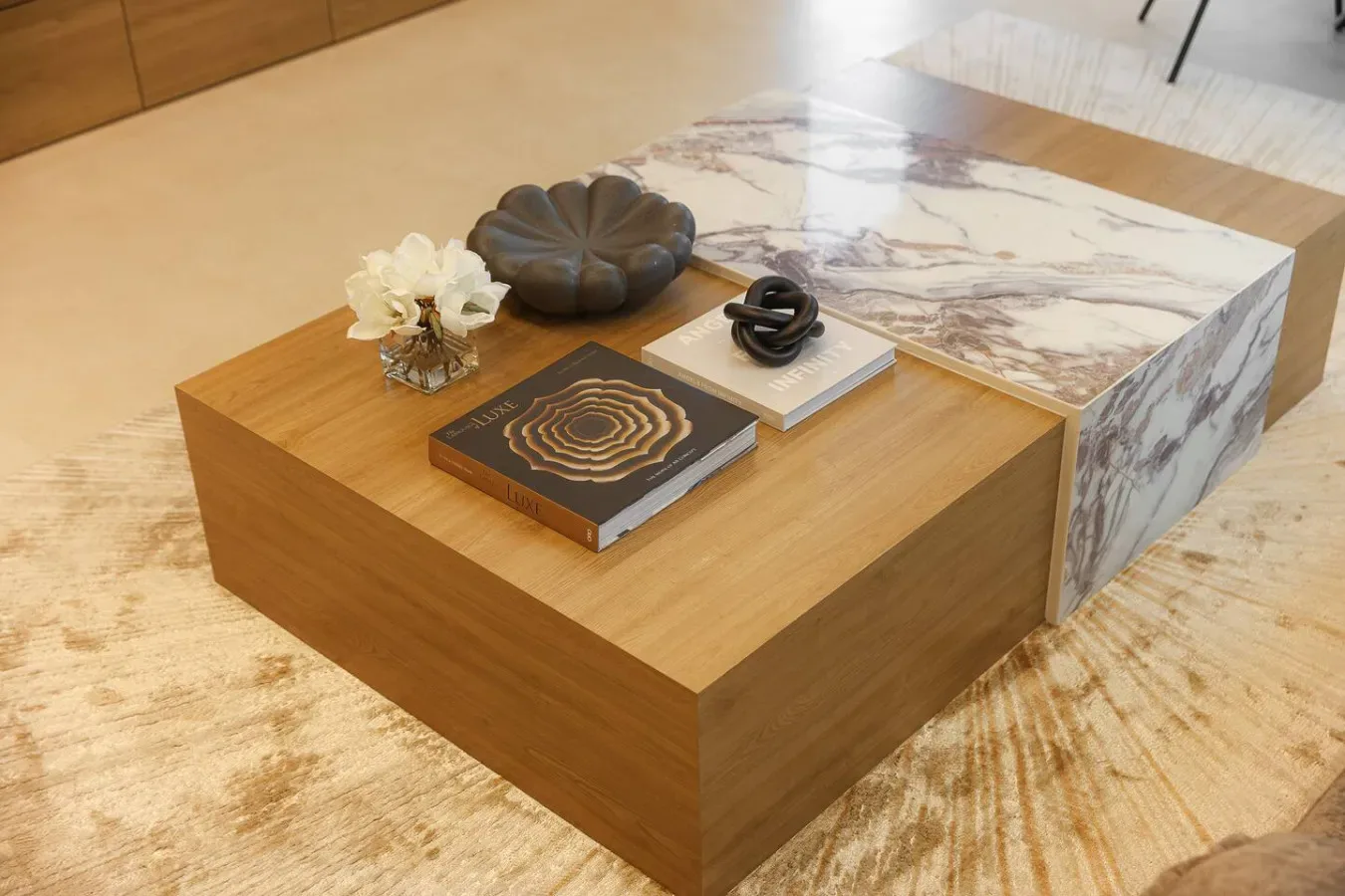 Una mesa de centro baja de madera sostiene objetos decorativos junto a una mesa con cubierta de mármol.