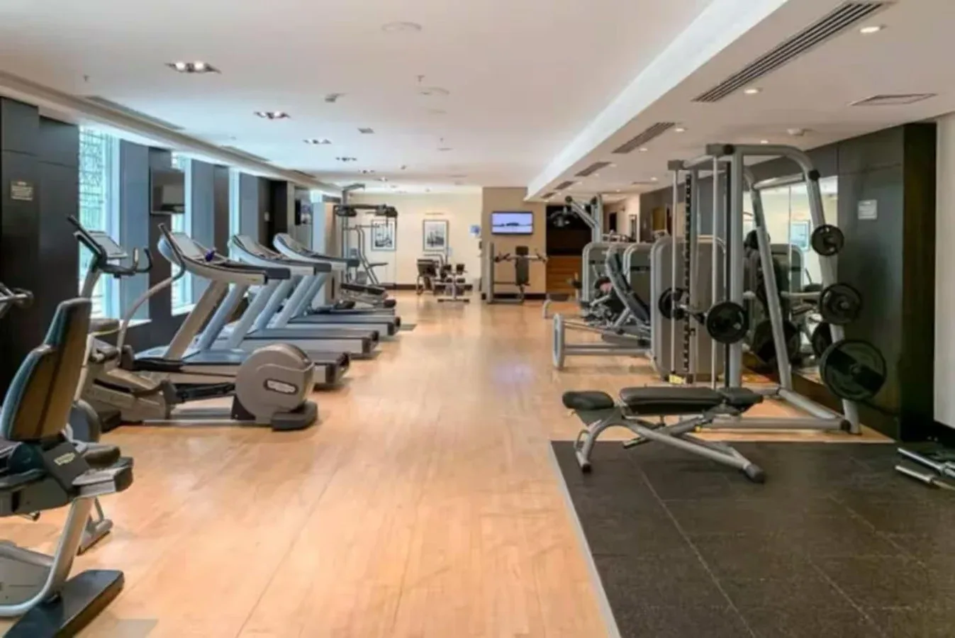 Un gimnasio con máquinas de cardio a un lado y equipo de entrenamiento con pesas al otro.
