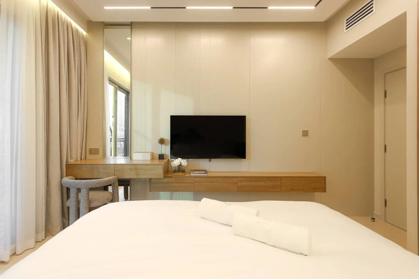 Dormitorio con una cama frente a un televisor montado en la pared y una consola larga de madera.