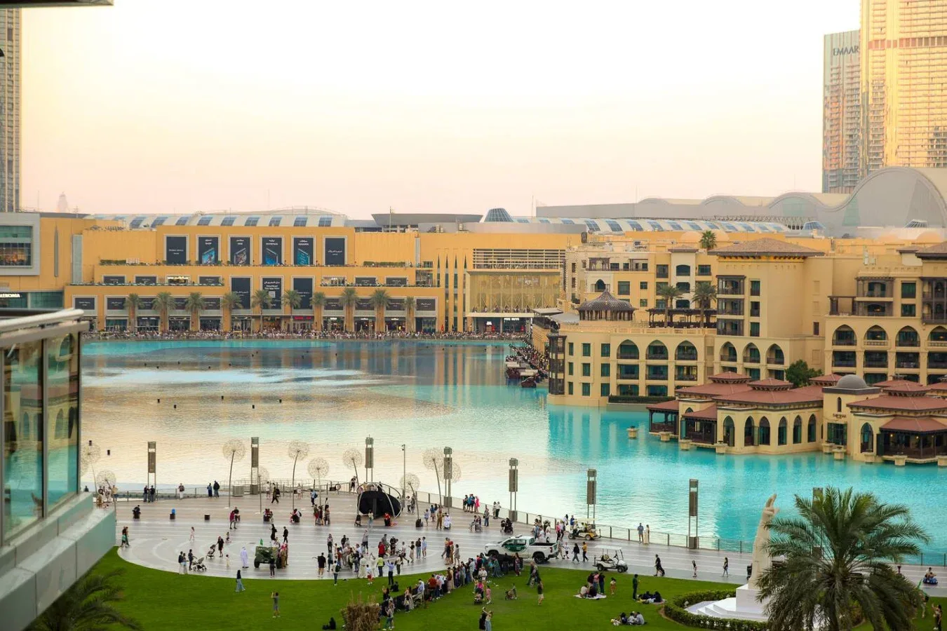 Una amplia piscina turquesa está junto a una plaza y grandes edificios.