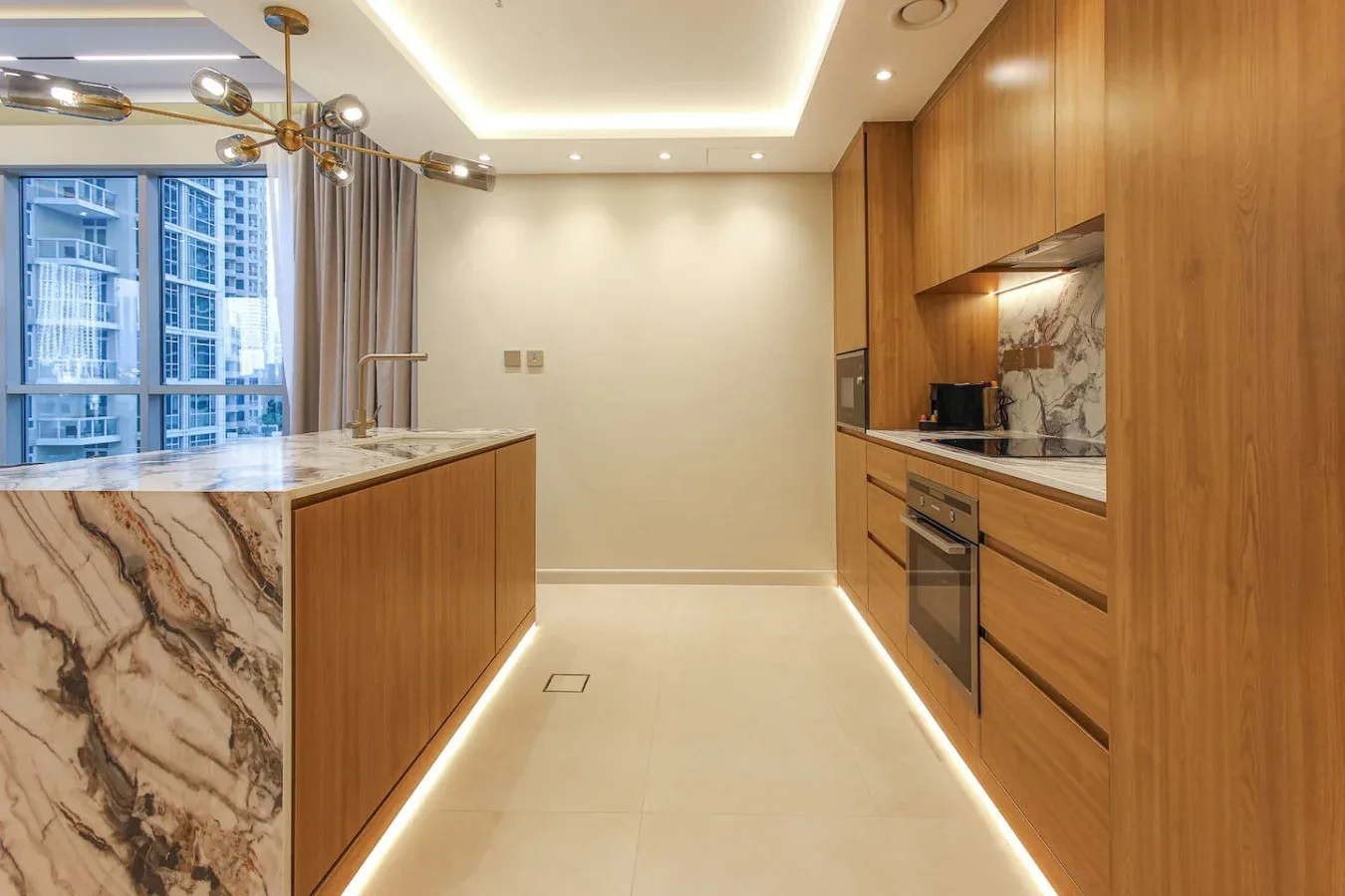 Una cocina moderna con gabinetes de madera, una isla de piedra y grandes ventanas.