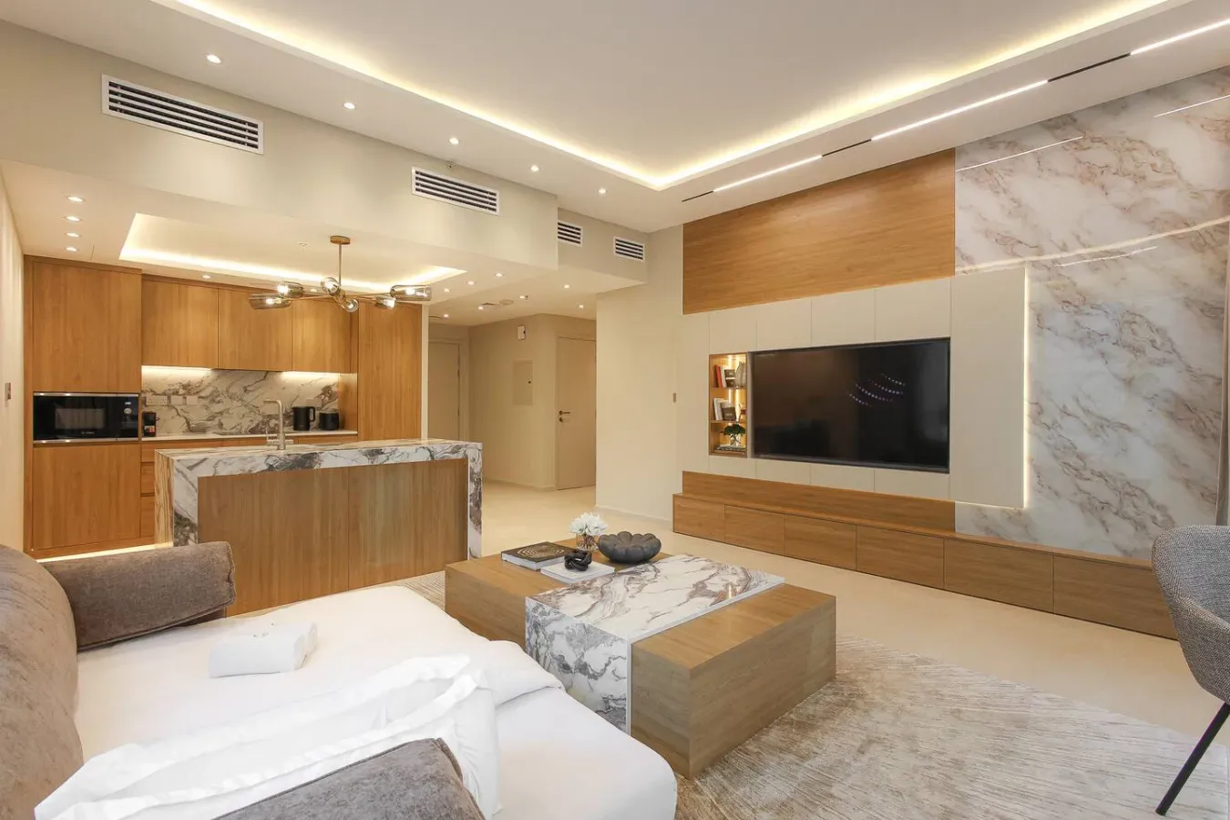 Una sala de estar moderna con una pared para televisión y una cocina abierta detrás de la zona de descanso.