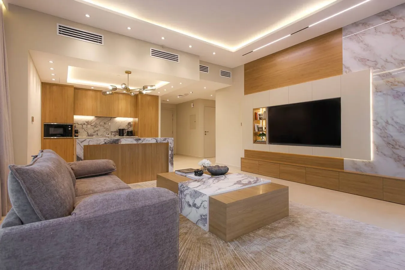 Una sala de estar moderna con asientos, un televisor y una cocina abierta.
