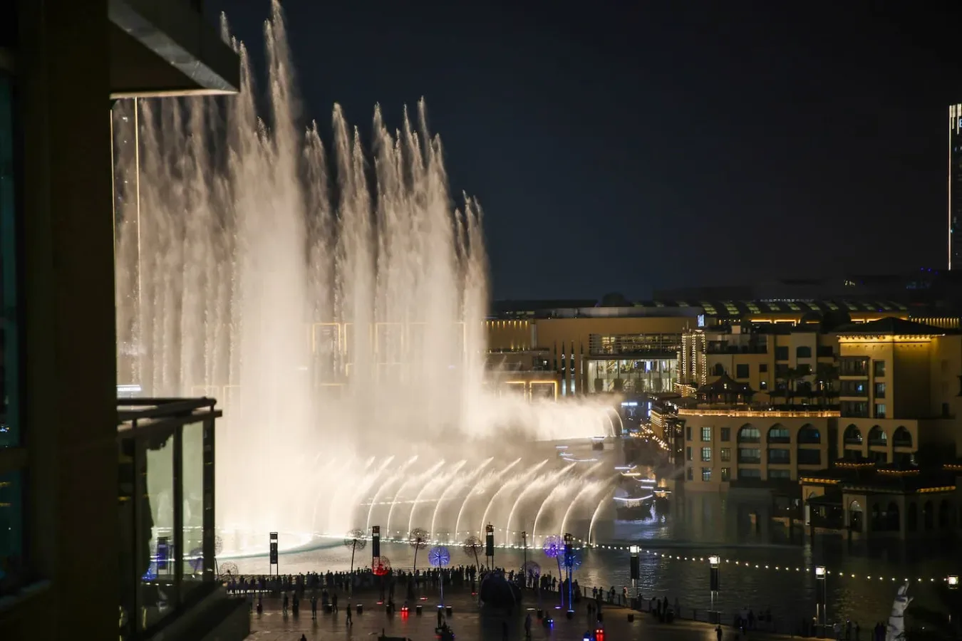 Un espectáculo nocturno de fuentes lanza chorros de agua iluminados frente a edificios.