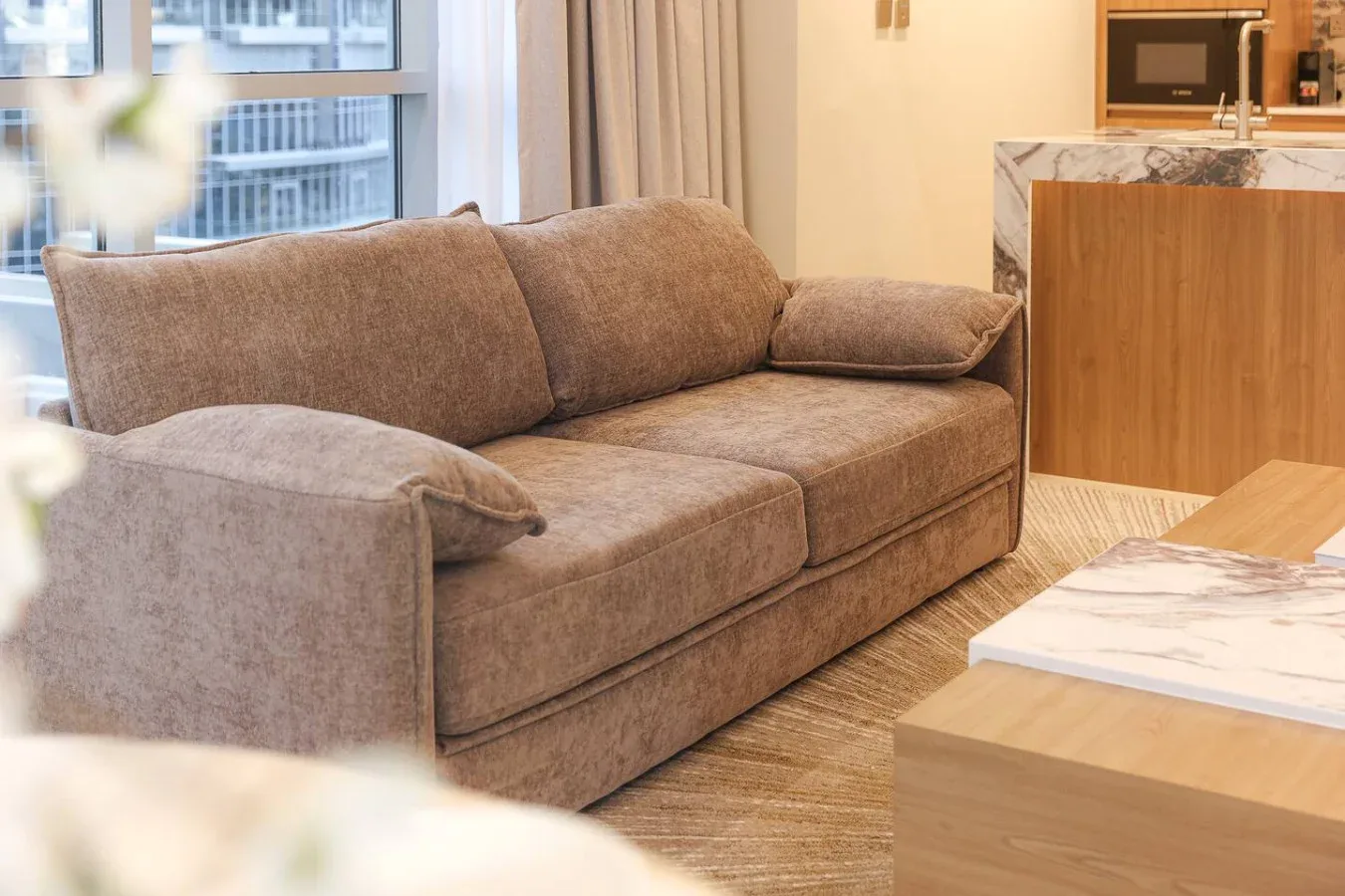 Una sala de estar con un sofá marrón junto a una isla de cocina revestida de madera.