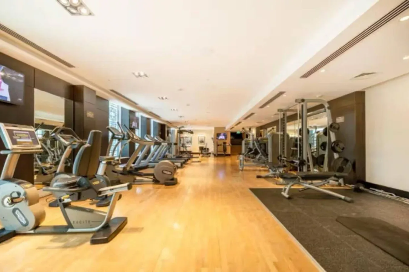 Un gimnasio con máquinas de ejercicio en una amplia sala con suelo de madera.