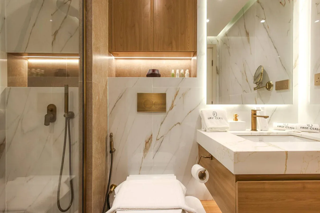 Un baño de mármol con ducha de vidrio, inodoro y tocador iluminado.