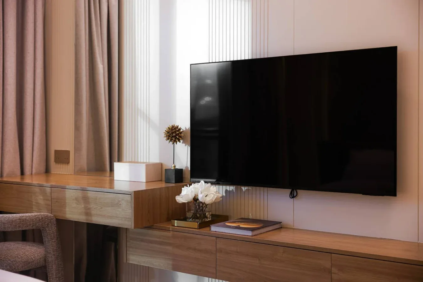 Una zona de estar tiene un televisor montado en la pared sobre un mueble de madera.