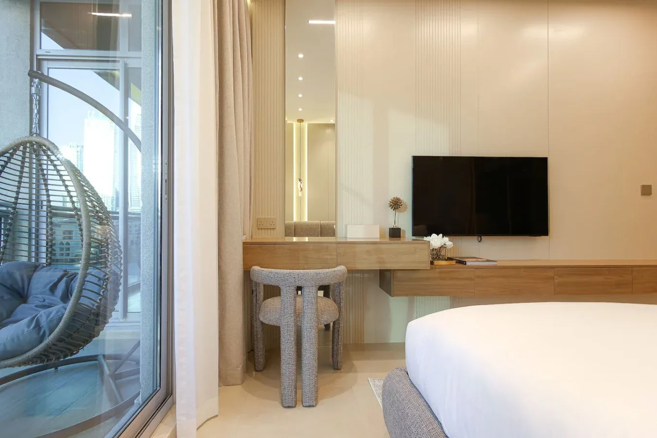 Dormitorio con cama, televisor en la pared y tocador junto a una ventana grande.