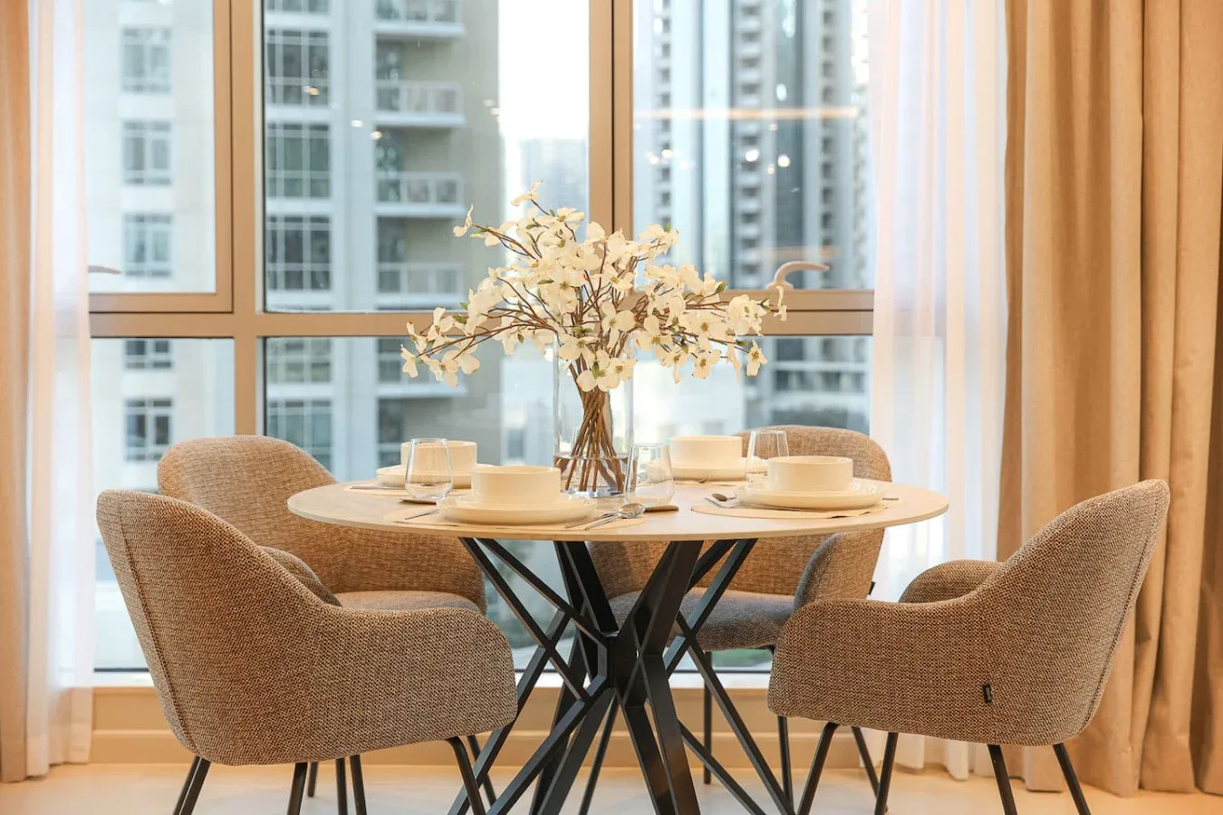 Comedor con una mesa redonda puesta junto a grandes ventanas.