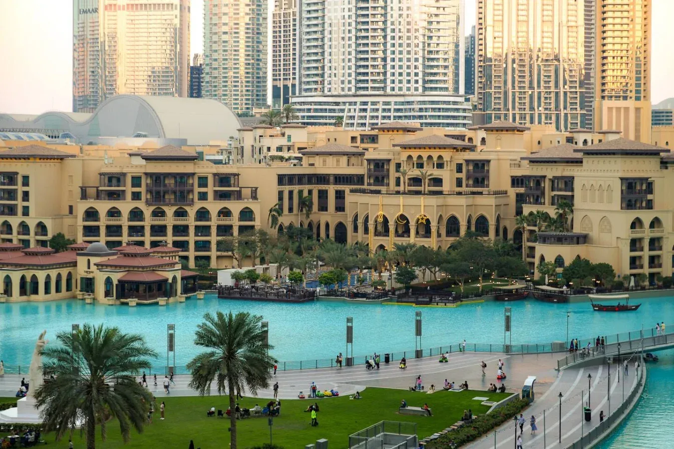 Una piscina turquesa y jardines se encuentran frente a un gran complejo de edificios.